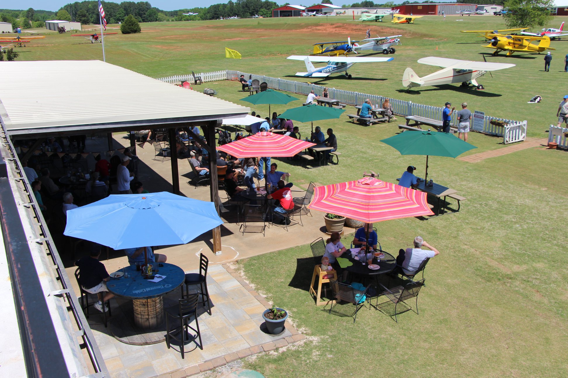 Outdoor dining tables beside vintage aircraft on the grass runway at Barnstormer's Grill.