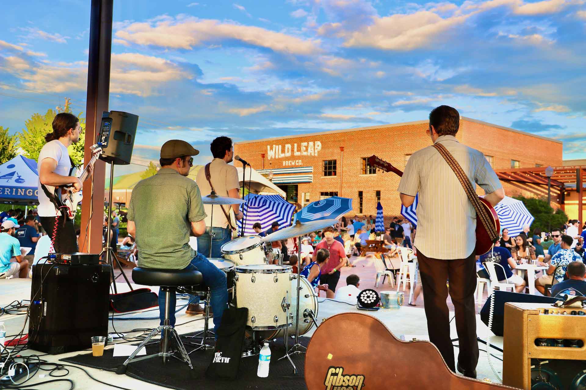 Outdoor performance in the courtyard at Wild Leap LaGrange, with the brick brewery building behind the stage.