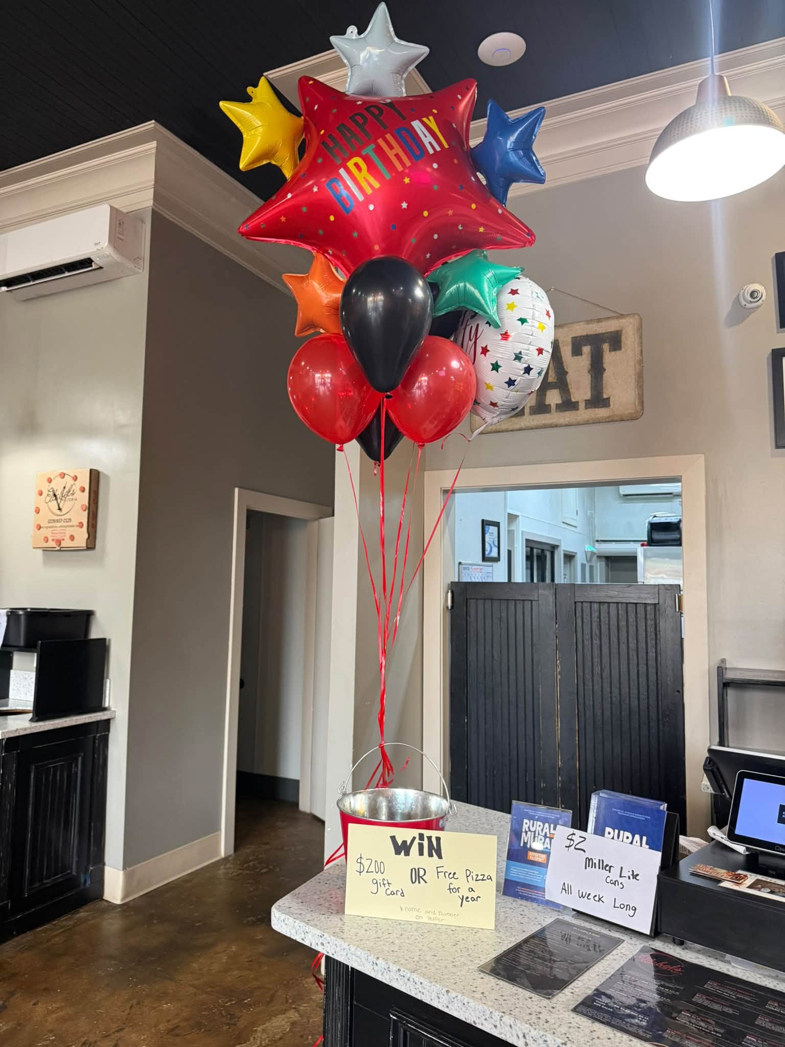 Front counter and dining-room interior at Ellabel's Pizzeria with temporary birthday balloons.