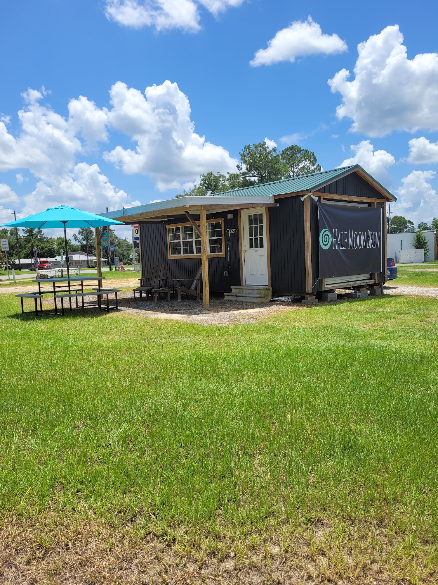 Half Moon Brew's dark-sided coffee shop with a green metal roof, name banner and outdoor picnic table.