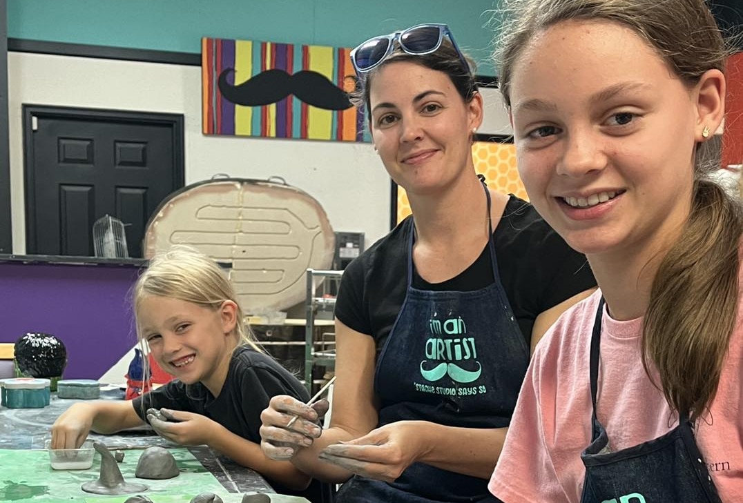 Participants shaping clay at a worktable inside Stache Studio.