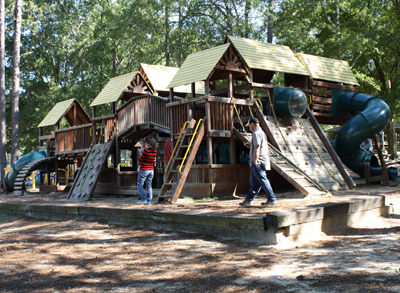 Wooden playground structures beneath tall trees at Partin Park in Lyons.