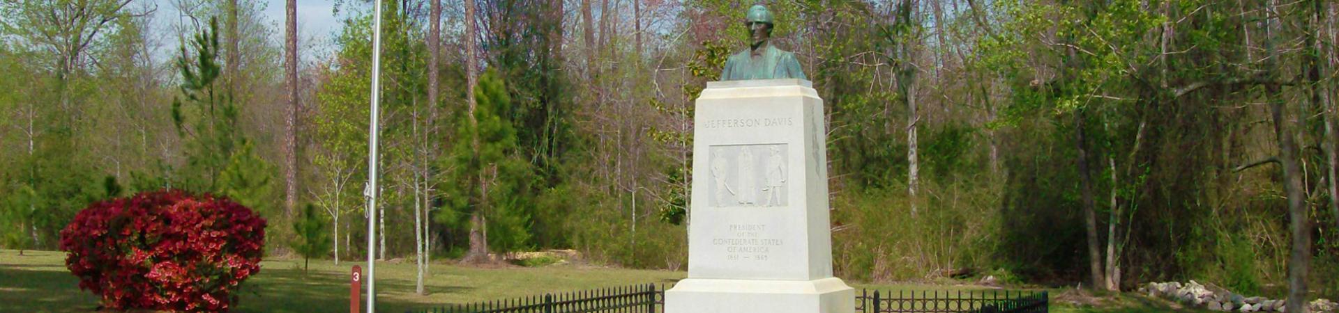 The monument, flagpole and wooded grounds at Jefferson Davis Memorial State Historic Site.