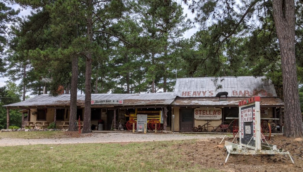Heavy's Bar-B-Que beneath pine trees, with Heavy's and Stella's Roadhouse signs.