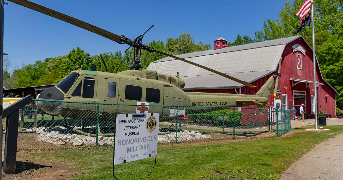 The red-barn Heritage Park Veterans Museum behind a displayed Huey helicopter and military flags.