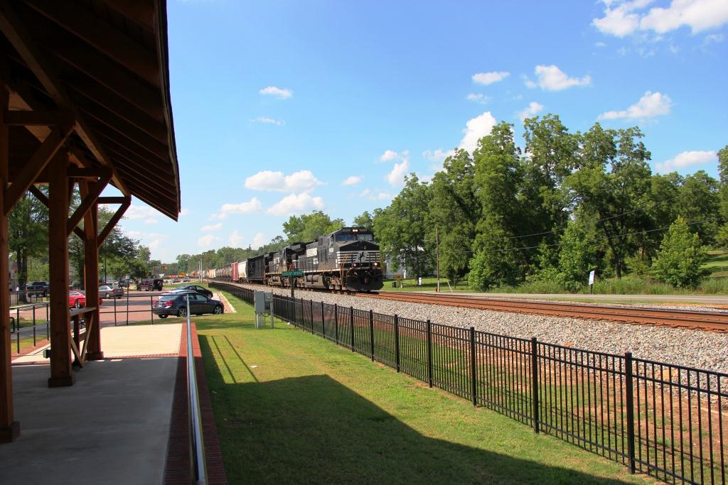 A Norfolk Southern freight train passing the covered Locust Grove train-watching platform and safety fence.