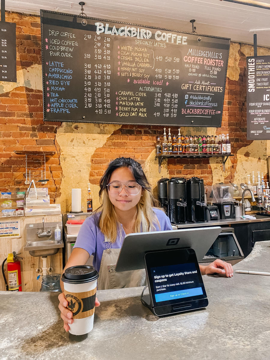 A Blackbird Coffee employee handing a cup across the signed downtown counter.