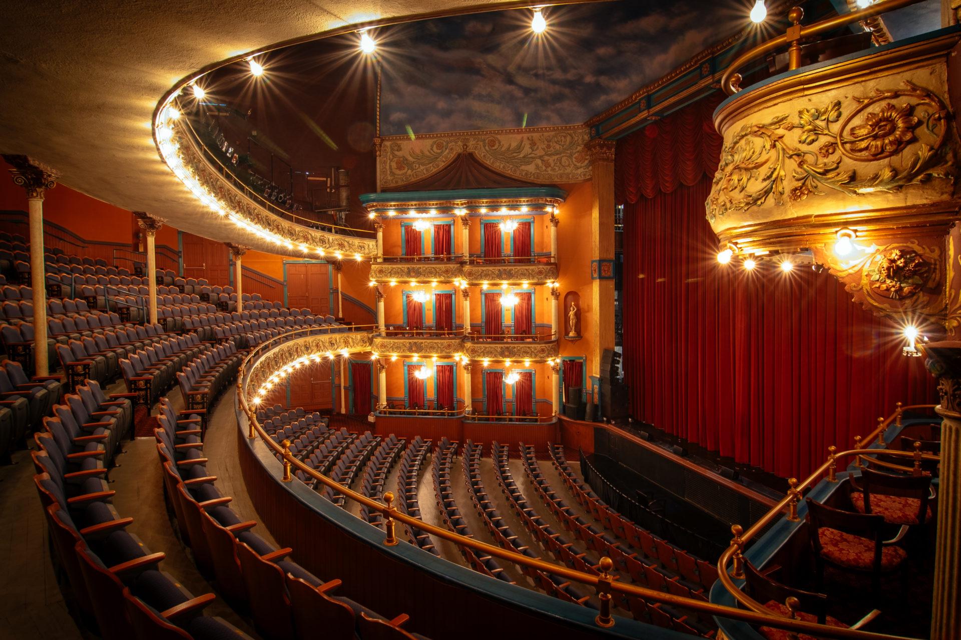 The Grand Opera House auditorium with its curved balcony, ornate theater boxes and red stage curtain.