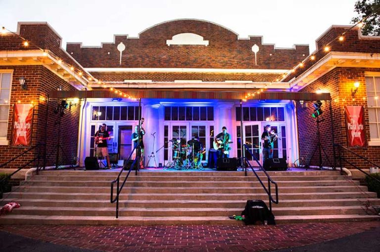 Musicians performing on the front steps of The Plaza Arts Center's brick schoolhouse building.