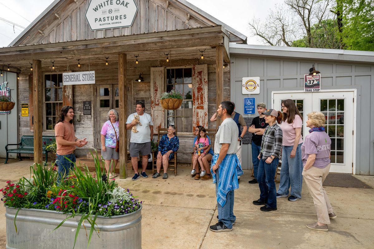 A guide speaking to a walking-tour group outside the signed White Oak Pastures General Store in Bluffton.