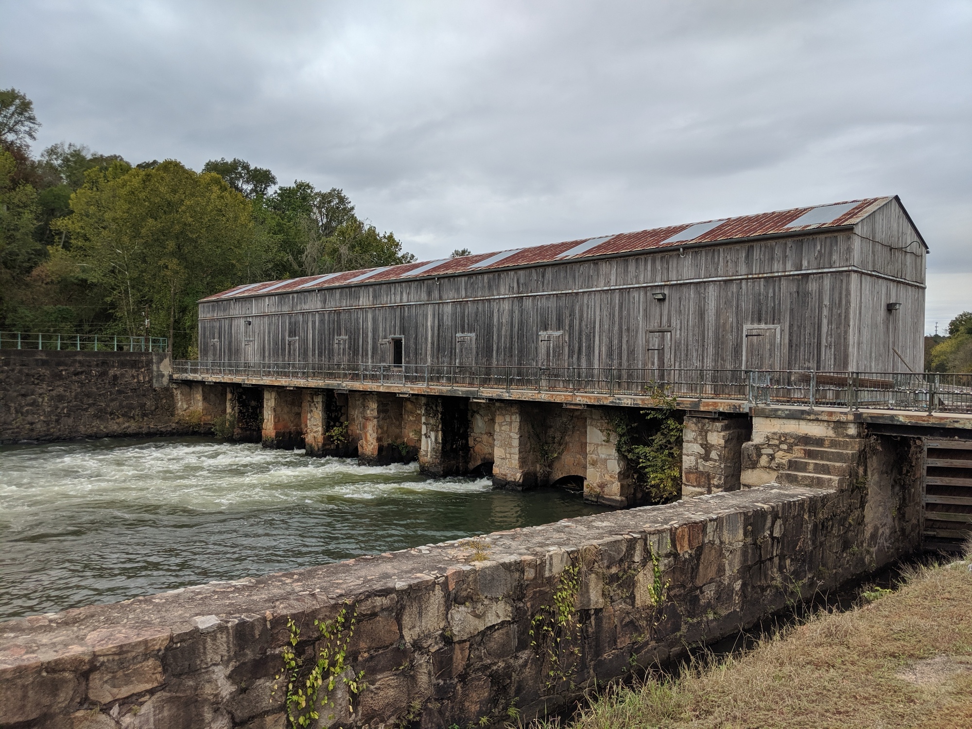 Historic wooden Augusta Canal headgates standing on stone piers above rushing water at Savannah Rapids Park.