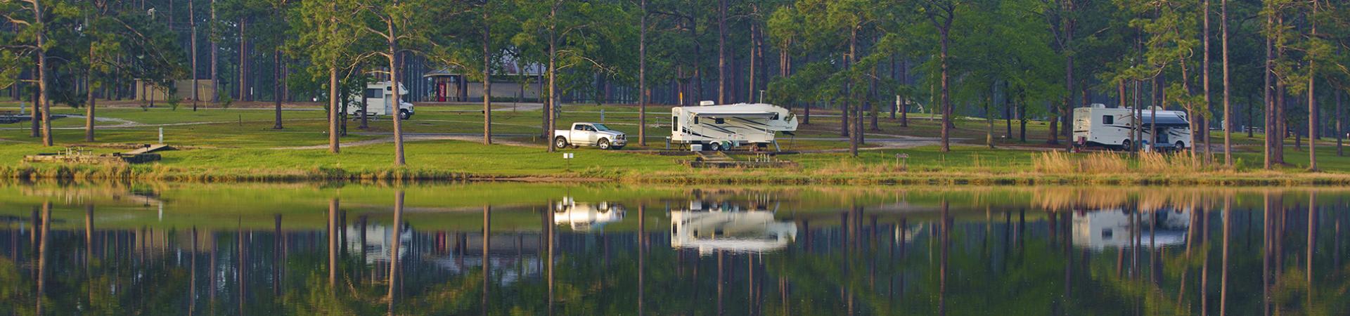 Lakefront campsites and RVs reflected in still water among tall pines at Seminole State Park.