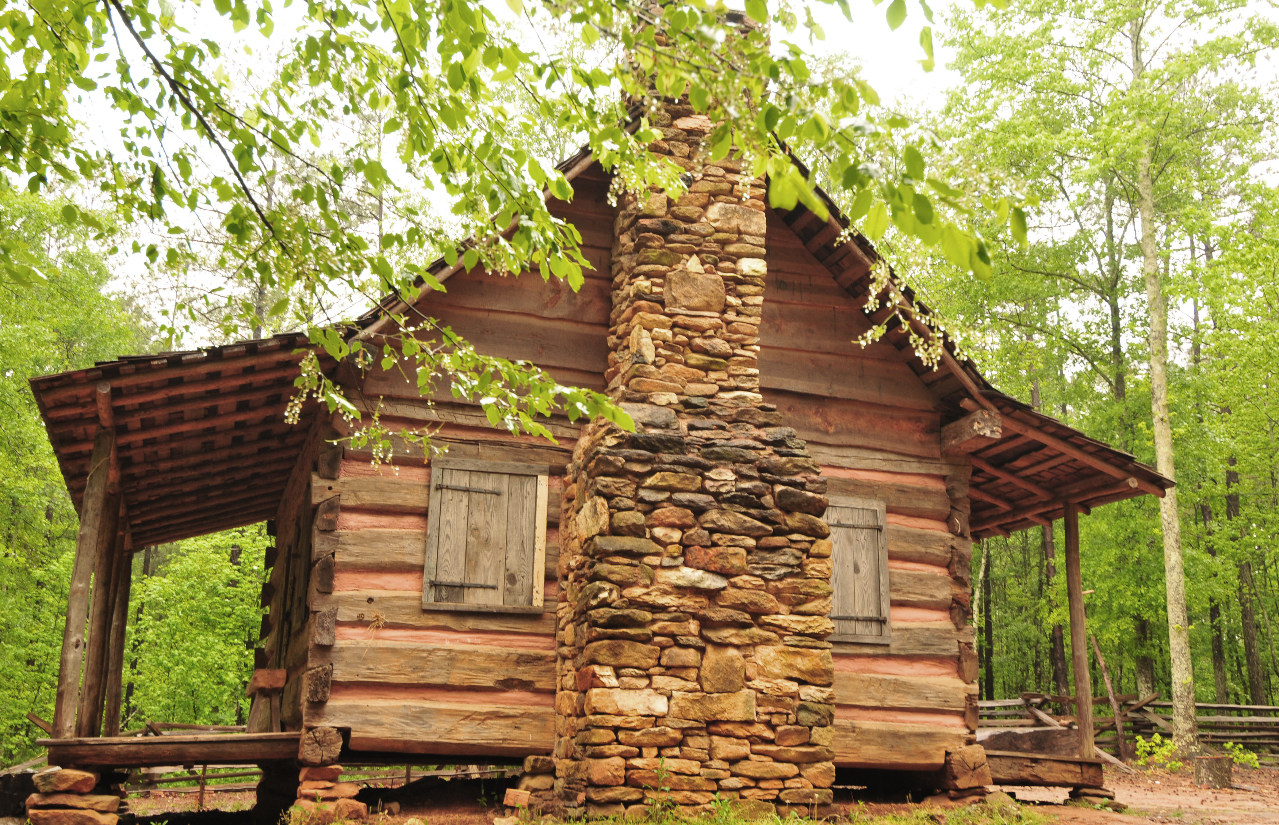 The reconstructed pioneer log cabin and stone chimney among trees at Pickett's Mill Battlefield.