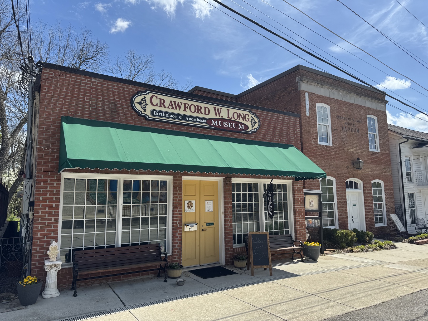 The brick Crawford W. Long Museum storefront with its sign and open flag in downtown Jefferson.