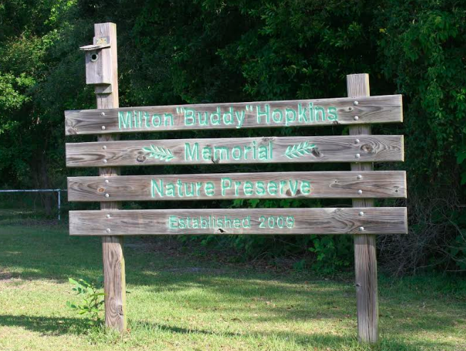 The wooden Milton Buddy Hopkins Memorial Nature Preserve sign and birdhouse at a wooded trail entrance.