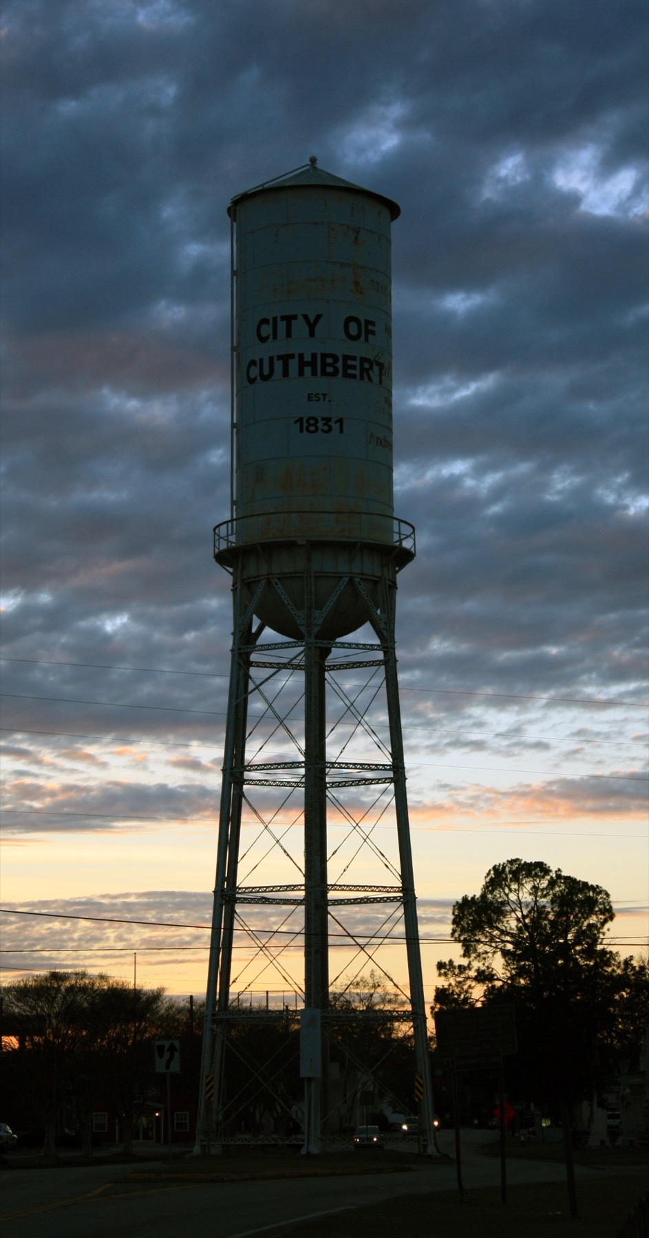 The tall riveted Cuthbert Water Tower with City of Cuthbert lettering between the divided roadway at dusk.