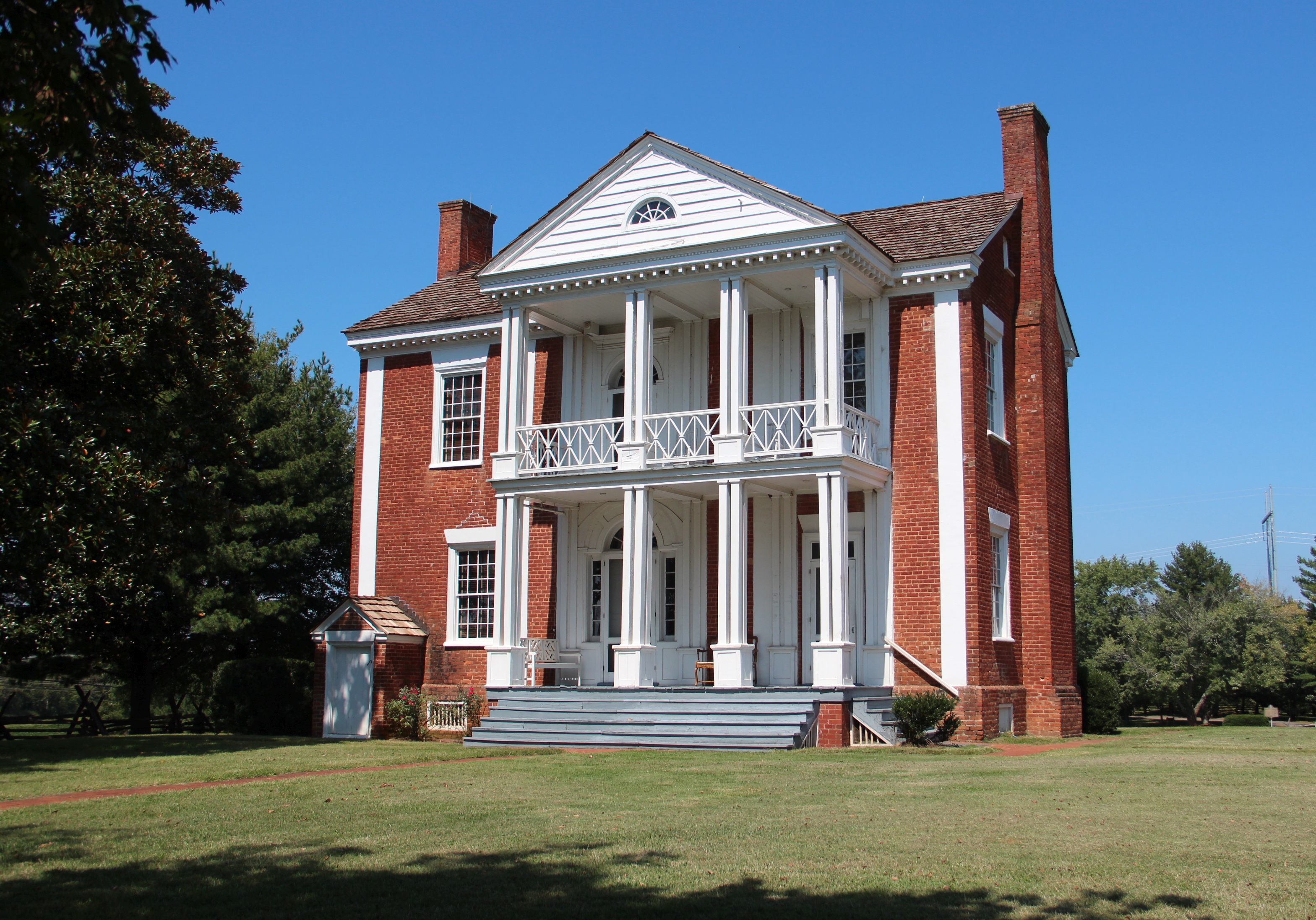 The red-brick Chief Vann House with white double porches and columns beyond a green lawn.