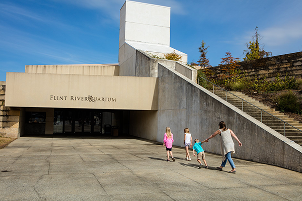 The signed Flint RiverQuarium entrance in downtown Albany with visitors walking toward the building.