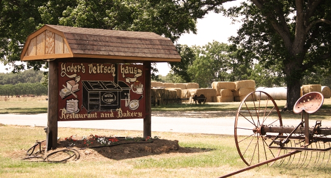 Yoder’s Deitsch Haus roadside sign with a farm wagon, trees and hay bales